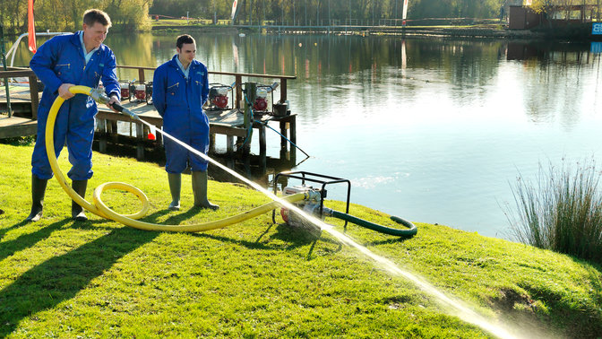 High pressure water pump being used by models in blue overalls - lake location.