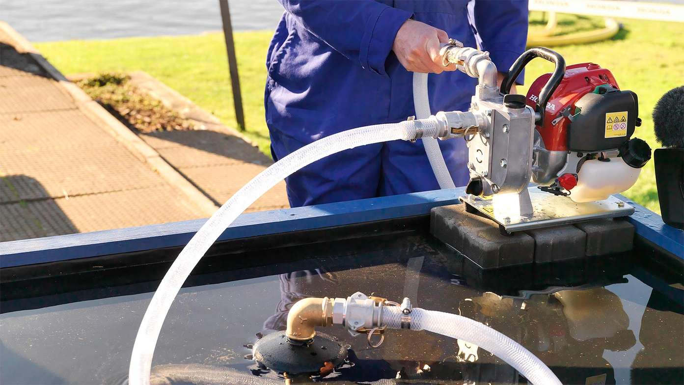 A man in blue overalls using lightweight water pump with Honda GX Series engine.