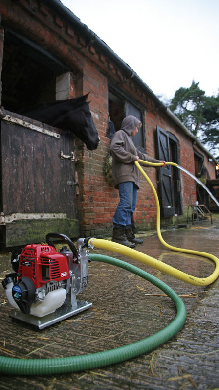 A woman using honda lightweight water pump outside of horse stable.