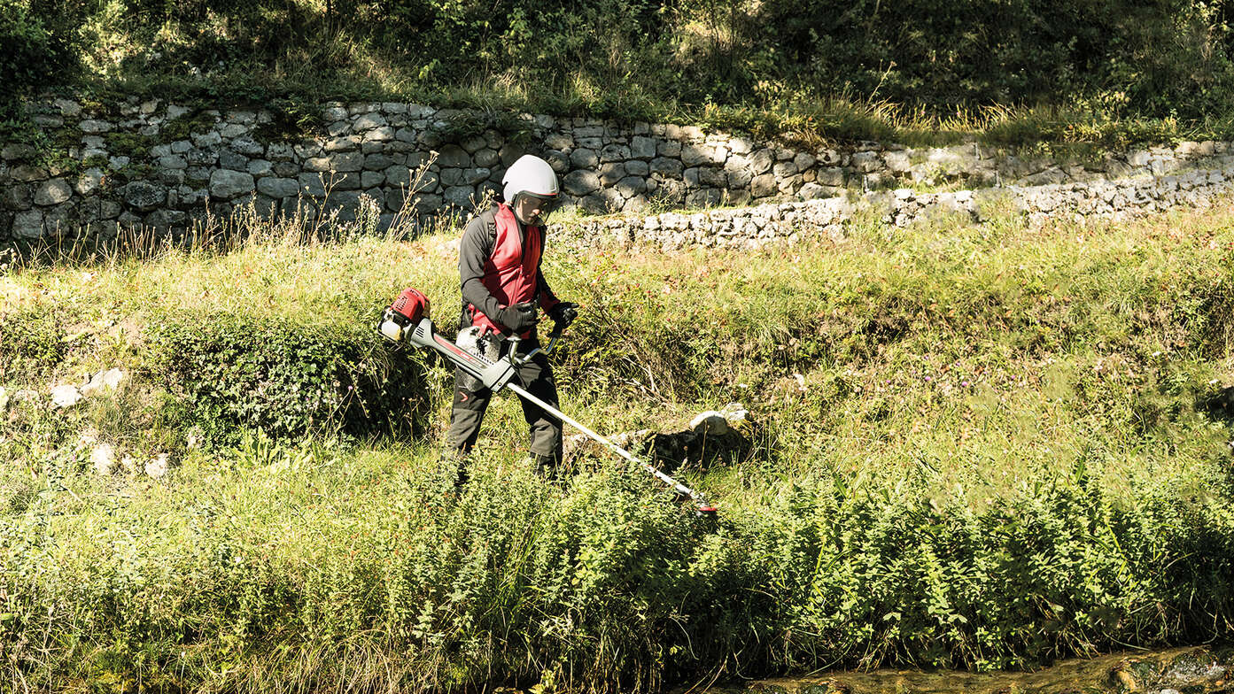 Brushcutter being used by man next to a stream