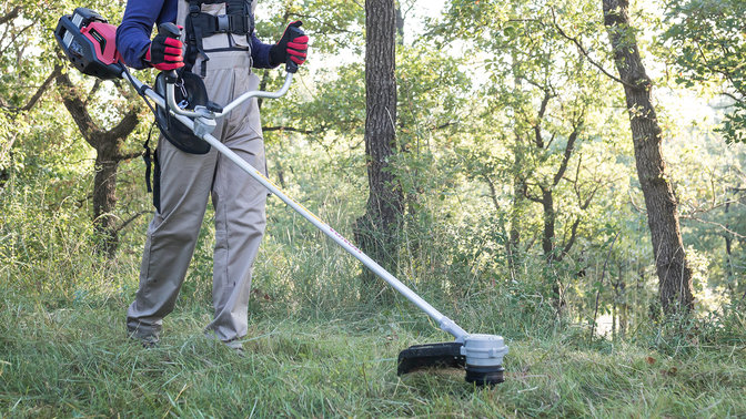 Front-three quarter view of brushcutter with model in a field.