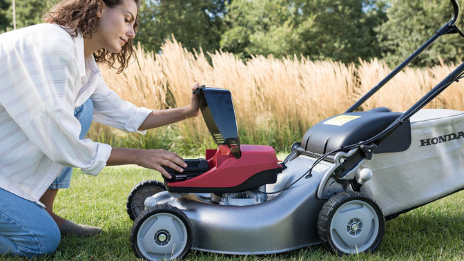 side view of woman removing rechargable battery from honda izy-on cordless lawn mower