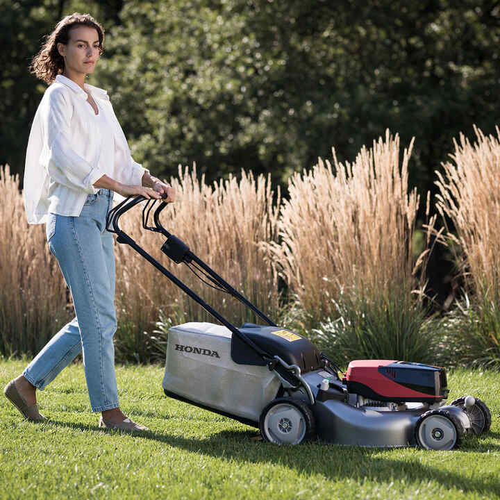 Woman pushing  IZY-ON lawnmower on the grass.