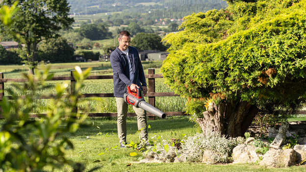 Man holding and using a Cordless Leafblower in garden