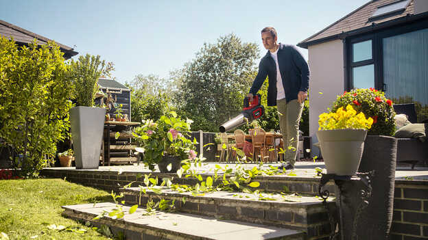 Man holding and using a Cordless Leafblower on patio