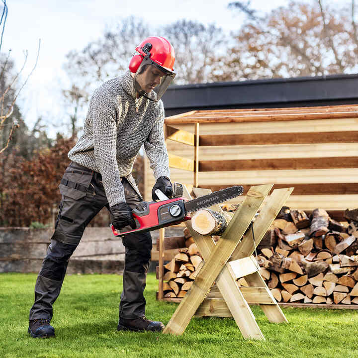 Man using a cordless chainsaw in a garden.