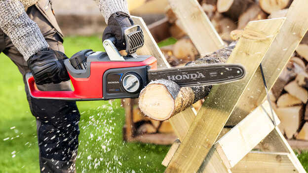 Man holding and using a Cordless Chainsaw in garden.