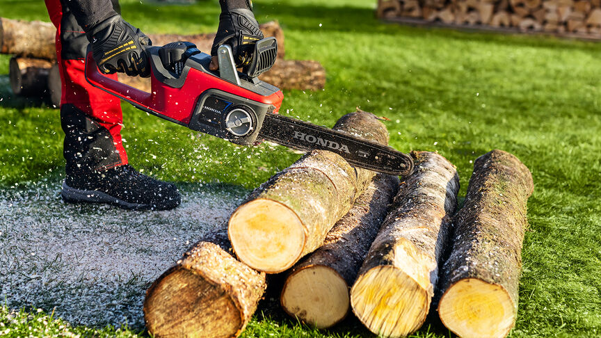 Close up of a model cutting wood with a Honda cordless chainsaw.
