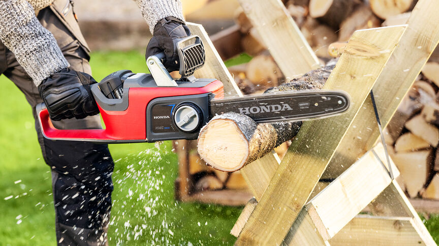 Close up of a model cutting wood with a Honda cordless chainsaw.