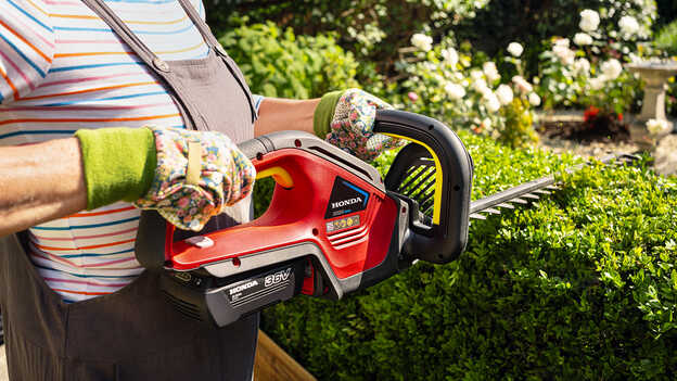 Close up of woman holding the Honda Cordless Hedgetrimmer in a garden location.