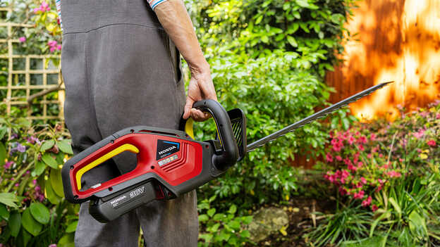 Model holding Honda Cordless Hedgetrimmer in a garden location.