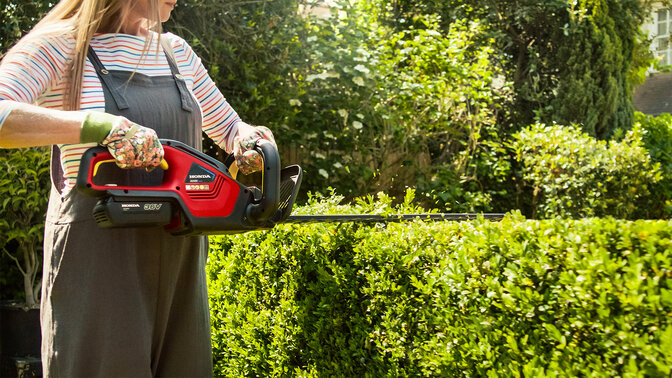 Lady with Honda Cordless Hedgetrimmer cutting hedge in garden location