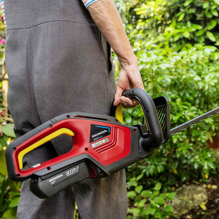 Model holding Honda Cordless Hedgetrimmer in garden location.