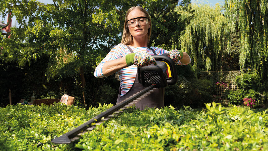 Woman using Honda Cordless Hedgetrimmer to cut hedge in garden location.