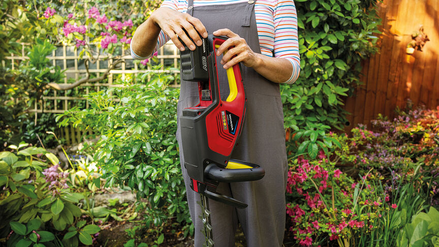 Woman using Honda Cordless Hedgetrimmer to cut hedge in garden location.