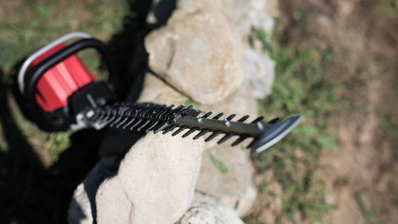 Front top view of Honda cordless hedge trimmer leaning on a stone wall.