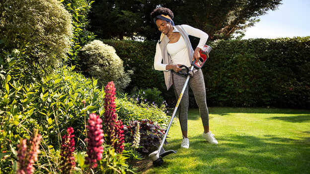 Woman using Honda Cordless lawntrimmer on grass in a garden location demonstrating plant protection.
