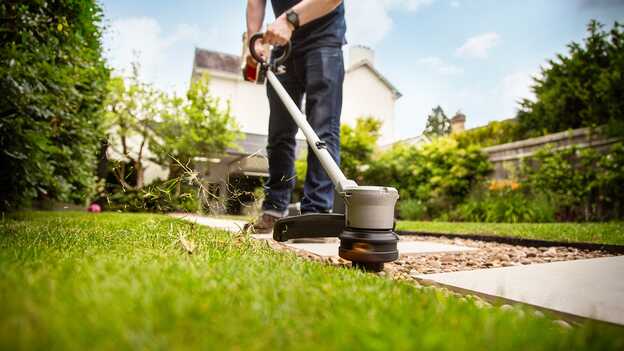 Man using Honda Cordless lawntrimmer on grass in a garden location.