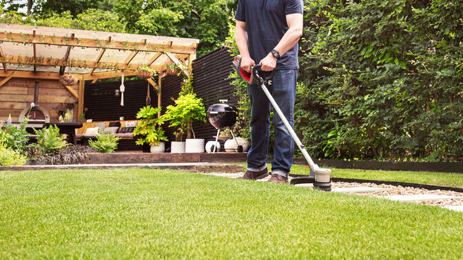 Man with Honda Cordless Hedgetrimmer cutting grass in garden location.