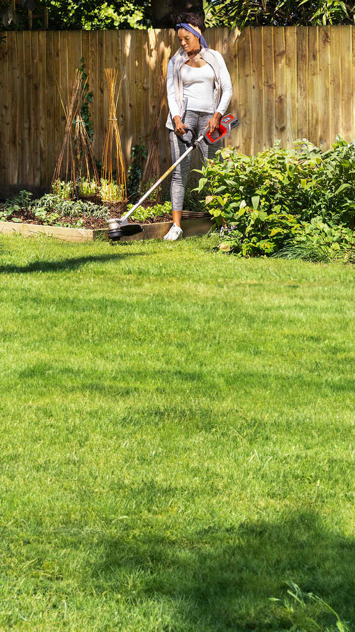 Model holding Honda Cordless Lawntrimmer in garden location.