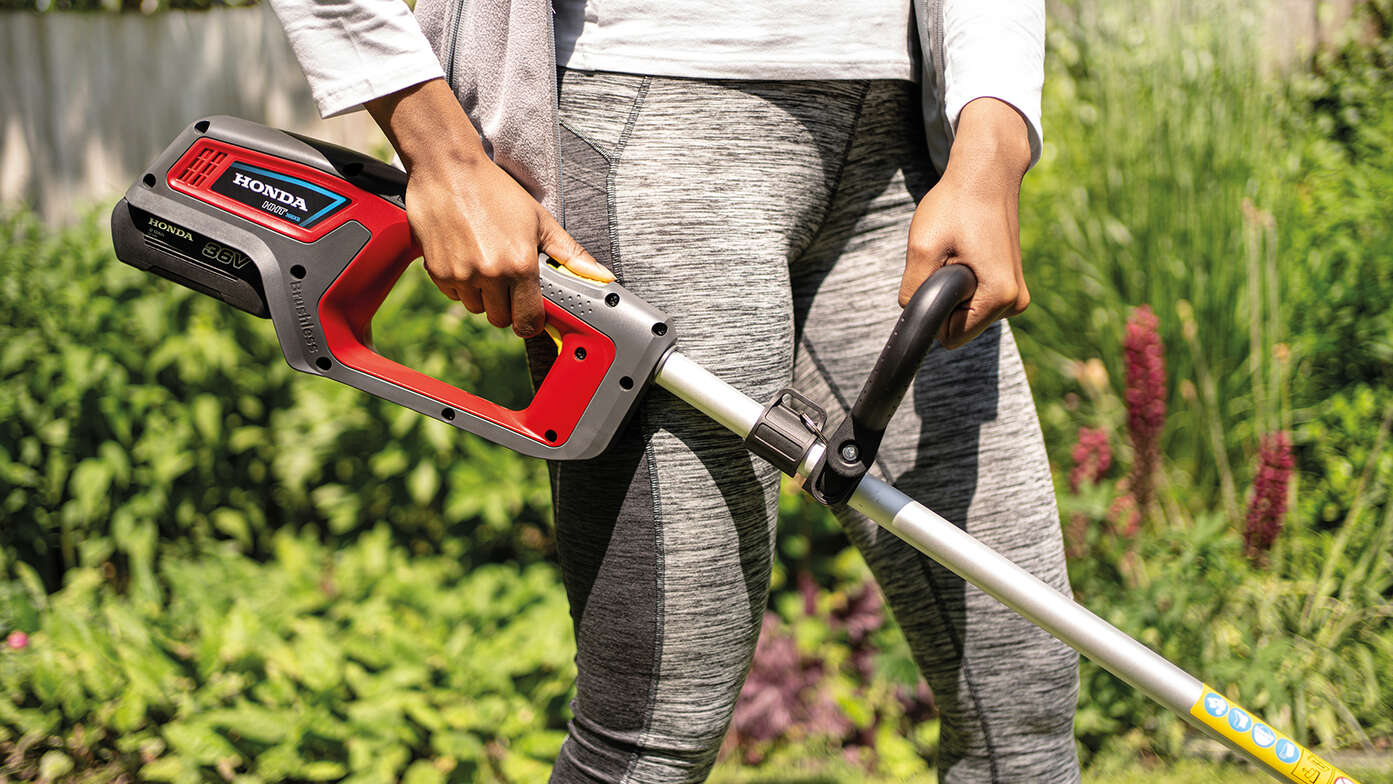 Close up of woman using Honda Cordless lawntrimmer in garden location.