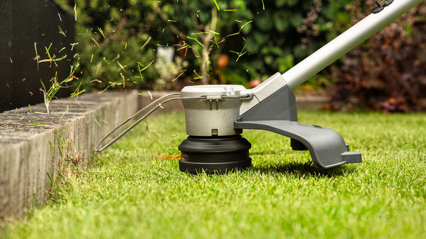 Honda Cordless lawntrimmer trimming side of grass in garden location.