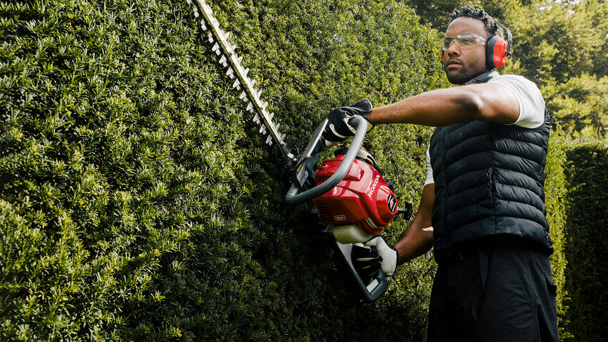Man using hedgetrimmer with noise cancellation headphones