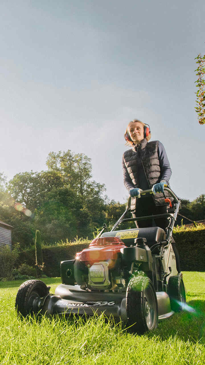 Man pushing HRH lawnmower in garden location.