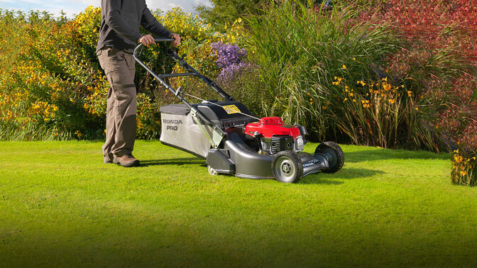 Man with Honda HRH lawnmower cutting grass in garden location