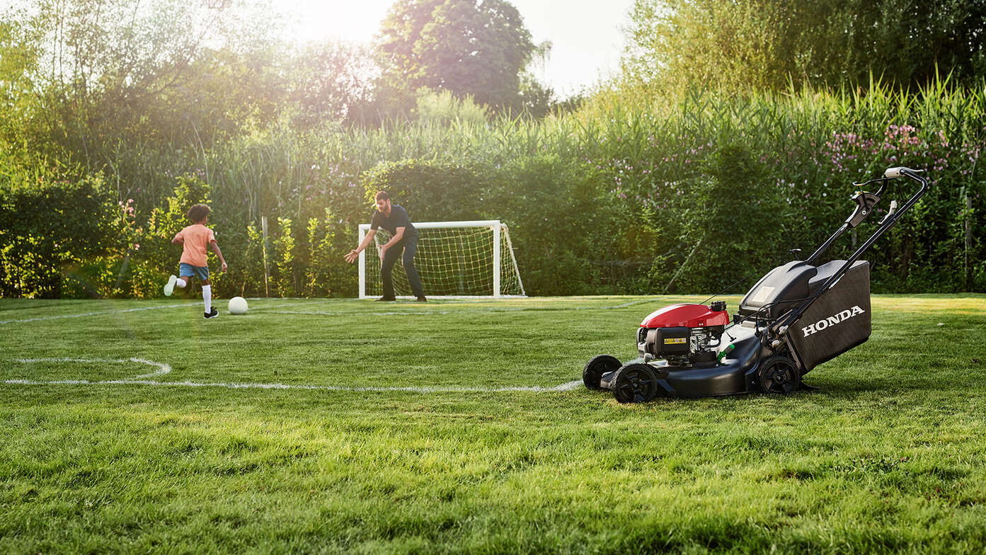 Man and child playing football beside side facing Honda HRN in the garden. 