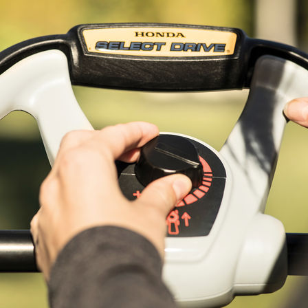 close-up of person using honda hrx petrol lawnmower select drive controls