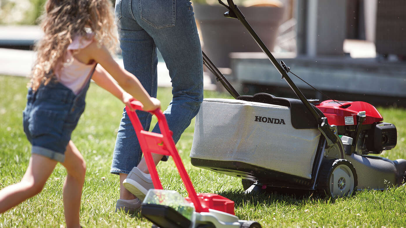 Honda IZY lawnmower side view with woman and child in garden location