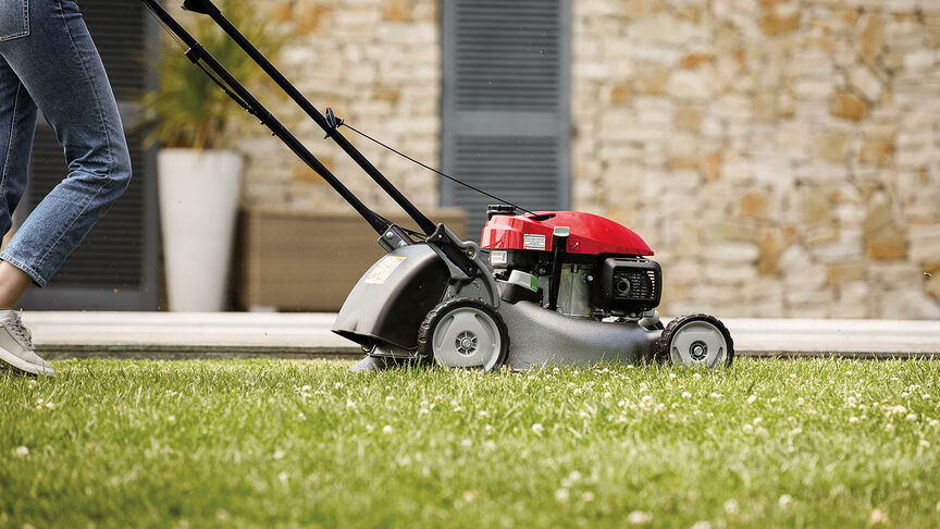 Honda IZY lawnmower side view with woman in garden