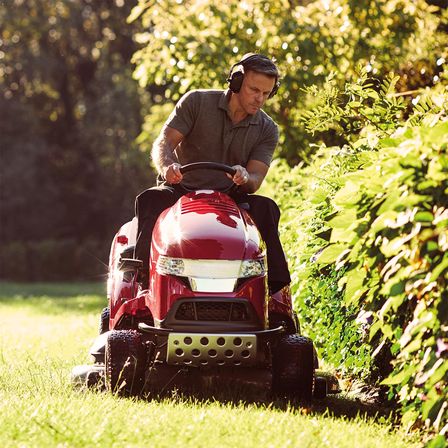 Premium lawn tractor, front three-quarter, left facing, being used by model, garden location.
