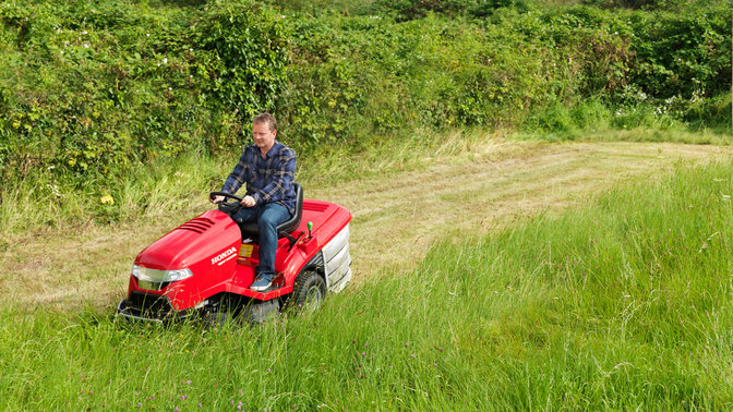 Premium lawn tractor, front three-quarter, left facing, being used by model, garden location.