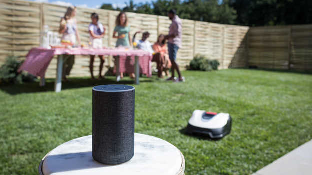 Close up of Amazon Alexa with Miimo and garden party in the background on the lawn.