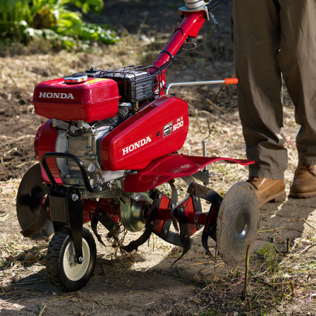 Close up of compact tiller, focusing on transport wheel, garden location.