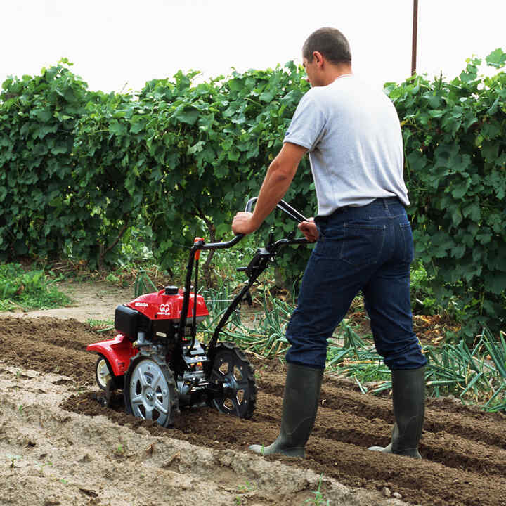 Man pushing rotary riller in field location