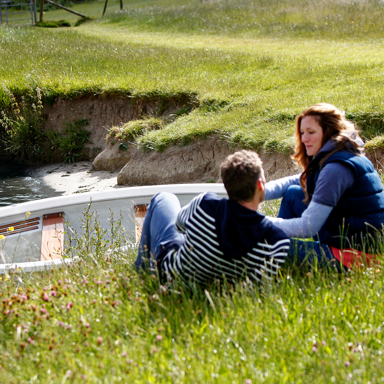 Twp people sitting on a river bank next to a boat in the water with a Honda BF2.3