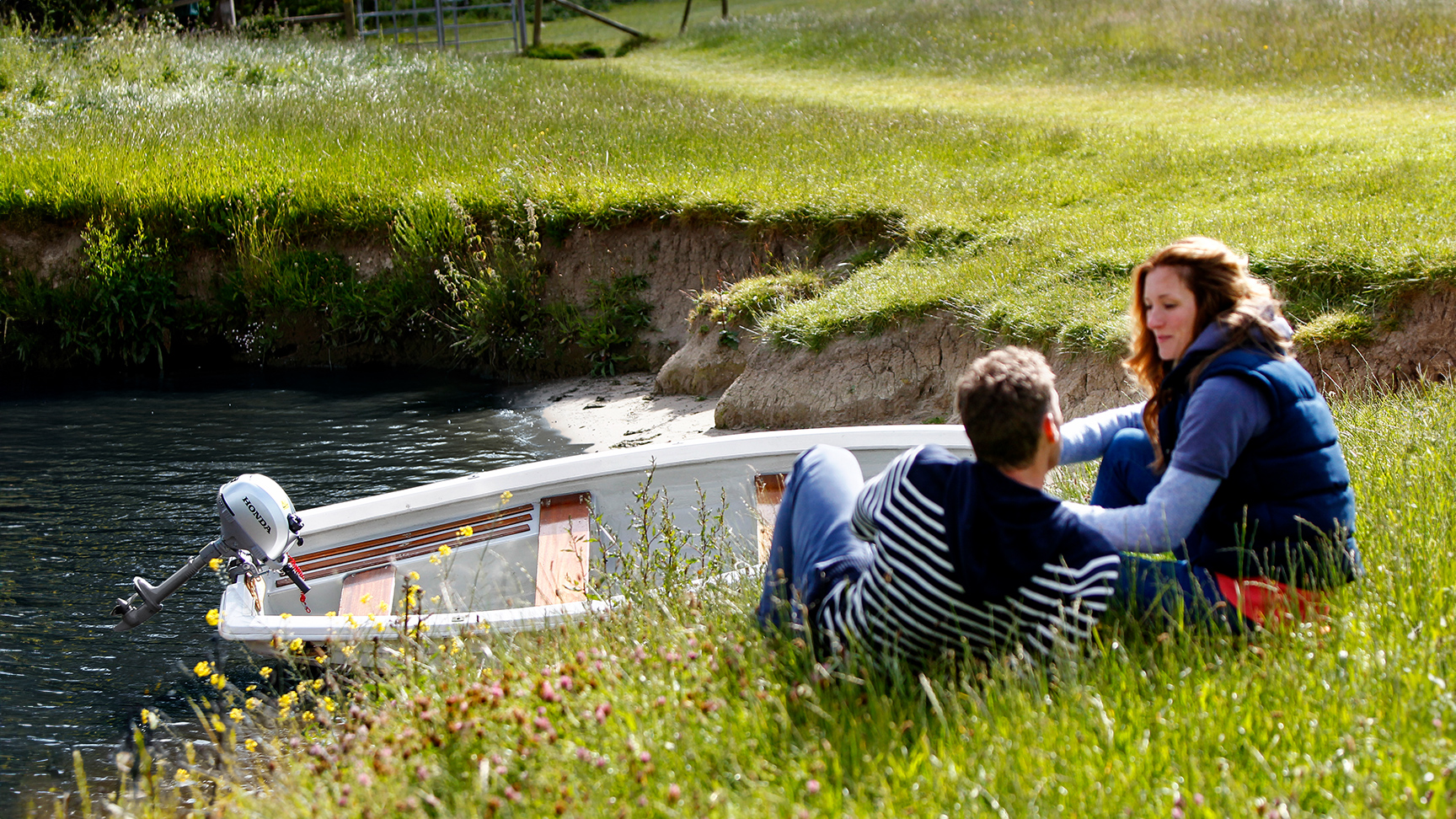 Twp people sitting on a river bank next to a boat in the water with a Honda BF2.3