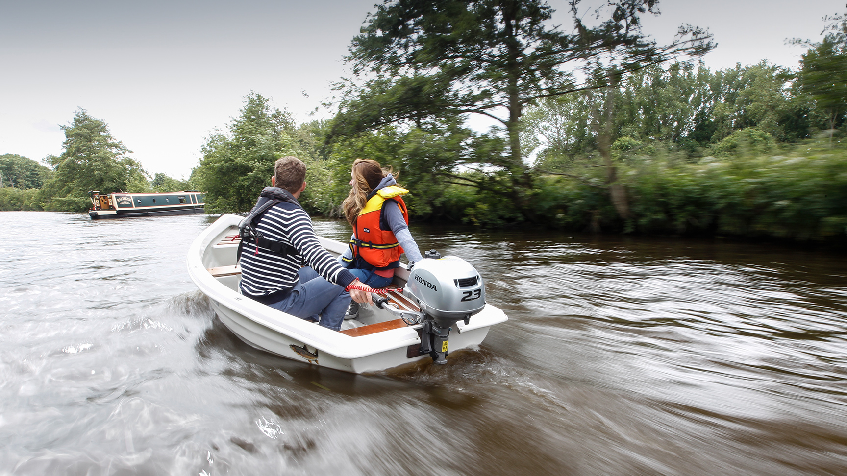 Two people in a boat using the Honda BF2.3 engine, next to a canal boat.