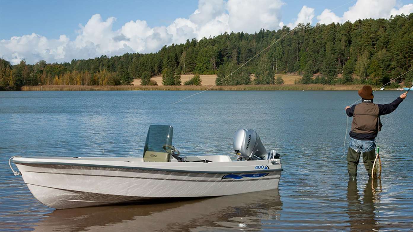 side view of boat with honda marine engine and man standing by its side fishing