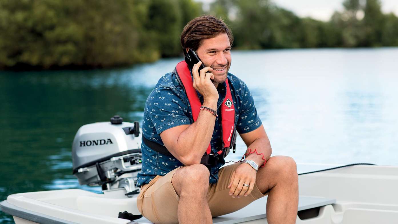 a man tallking on phone sat on boat fitted with a honda marine engine