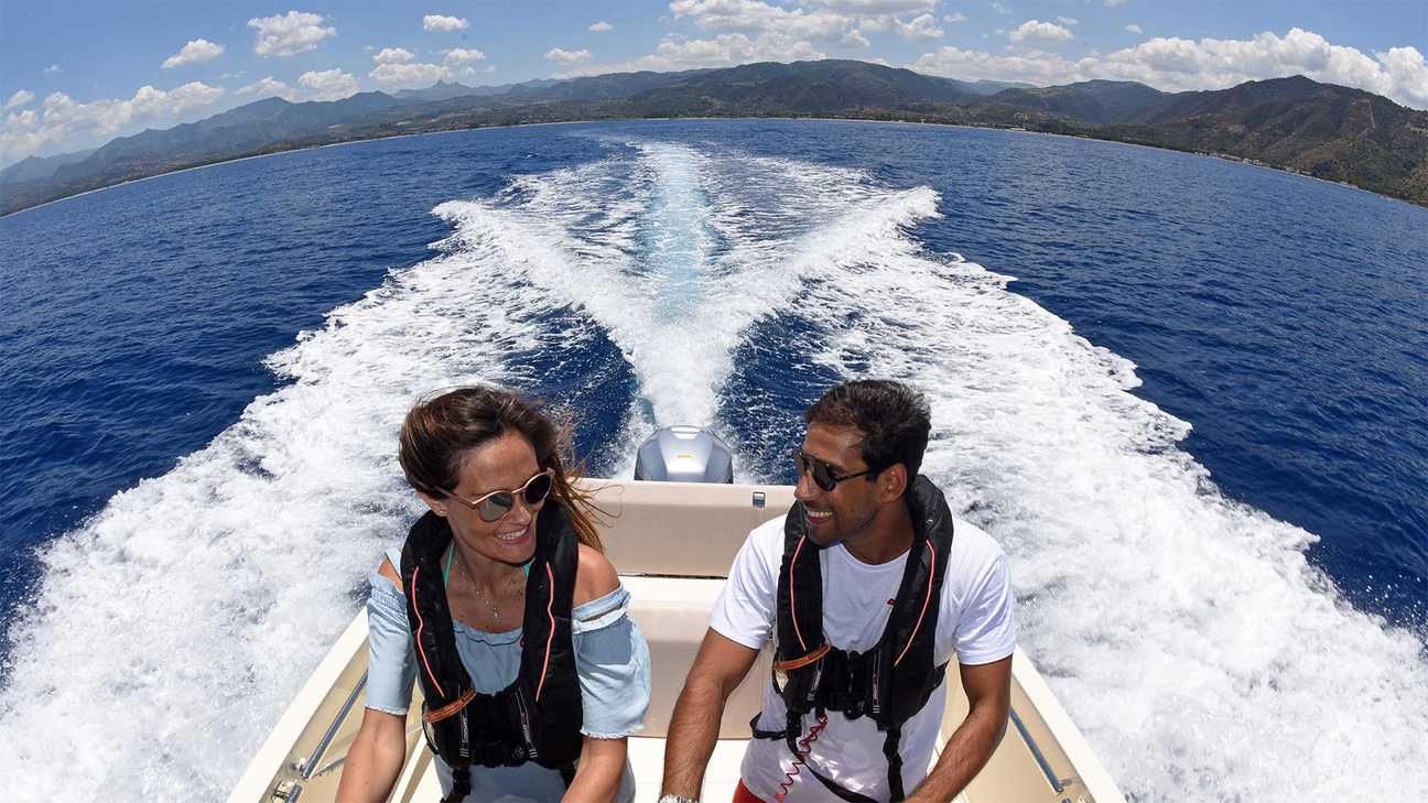 close up of couple steering a boat with the wake of the boat in the background