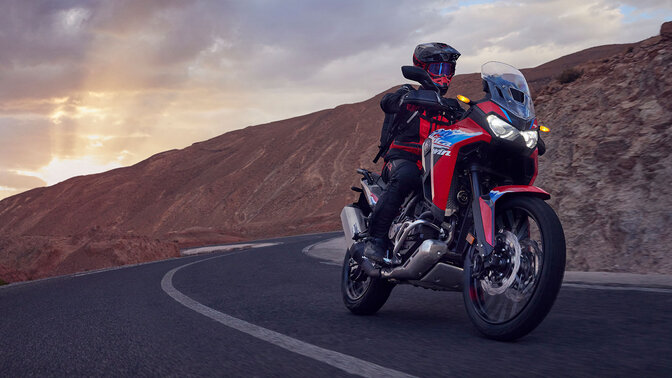 Model driving CRF1100L Africa twin motorbike on a road in a mountain location.