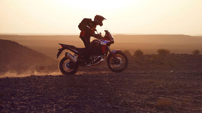 Model driving a CRF1100L Africa twin motorbike in a desert location.