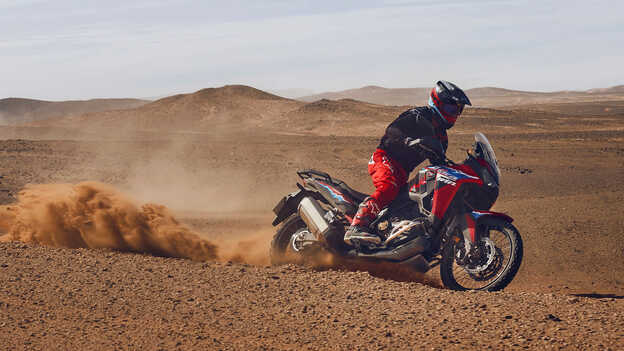 Model driving a CRF1100L Africa Twin motorbike in a desert location.