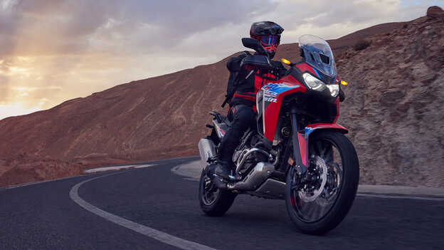 Model driving a CRF1100L Africa Twin bike in a desert location.