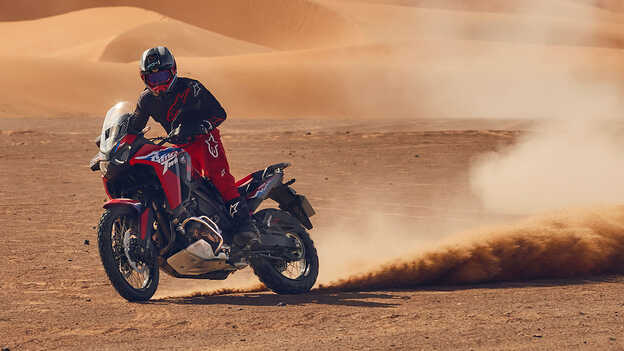 Model driving a CRF1100L Africa Twin bike in a desert location.