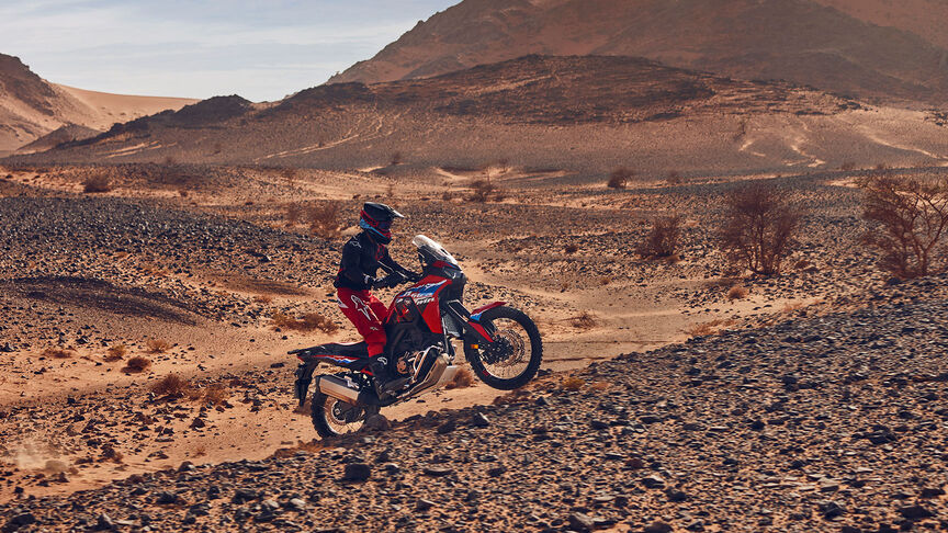 Model riding CRF1100L Africa Twin motorbike in a desert location.